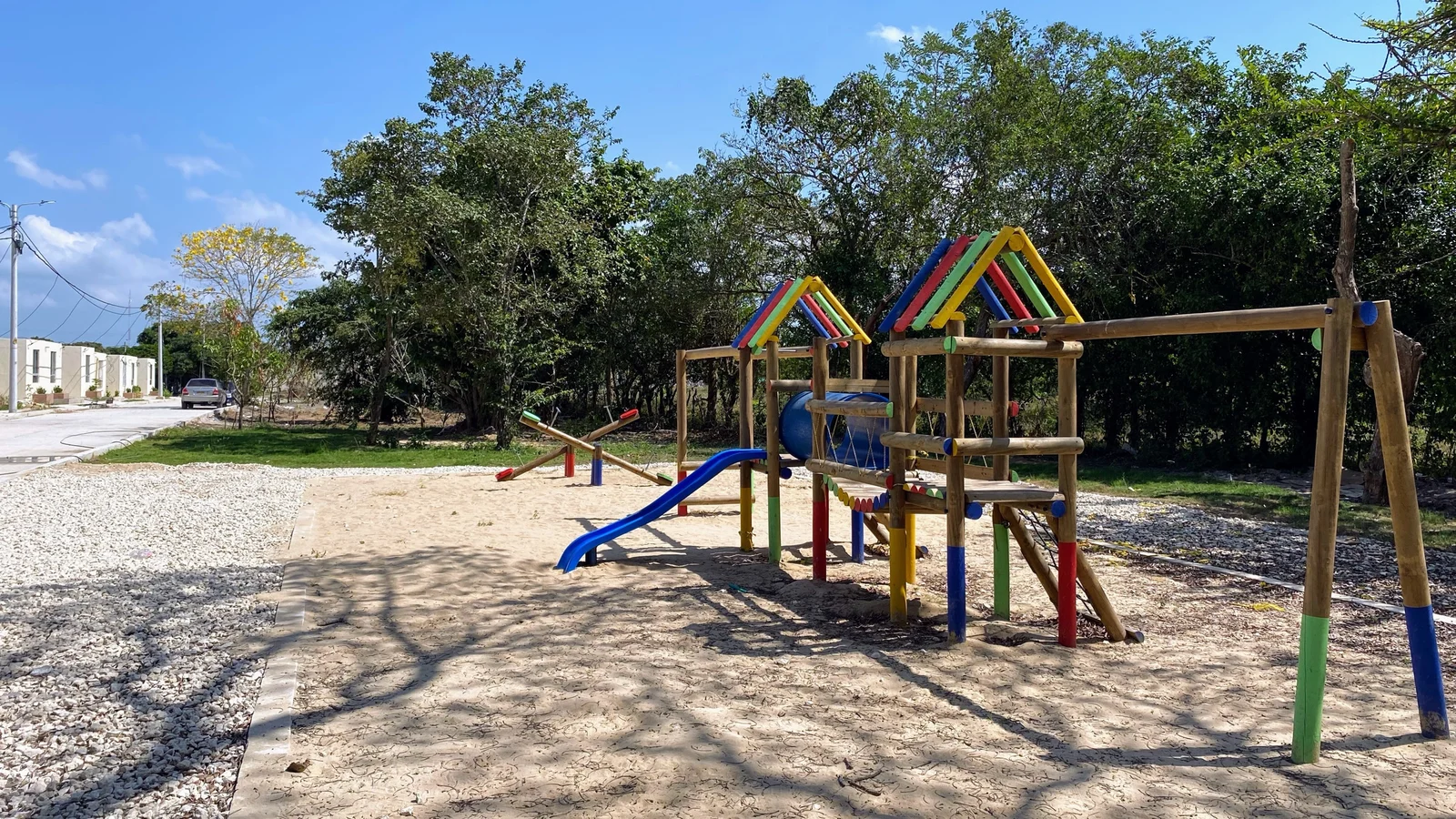 Parque infantil de San Antonio con resbaladera azul, estructura de madera y casas al fondo.